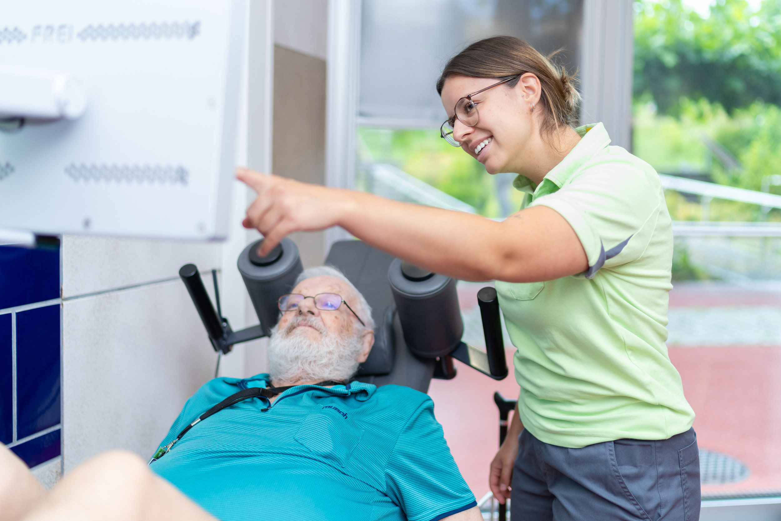 Therapeutin mit älterem Patienten an einem Trainingsgerät