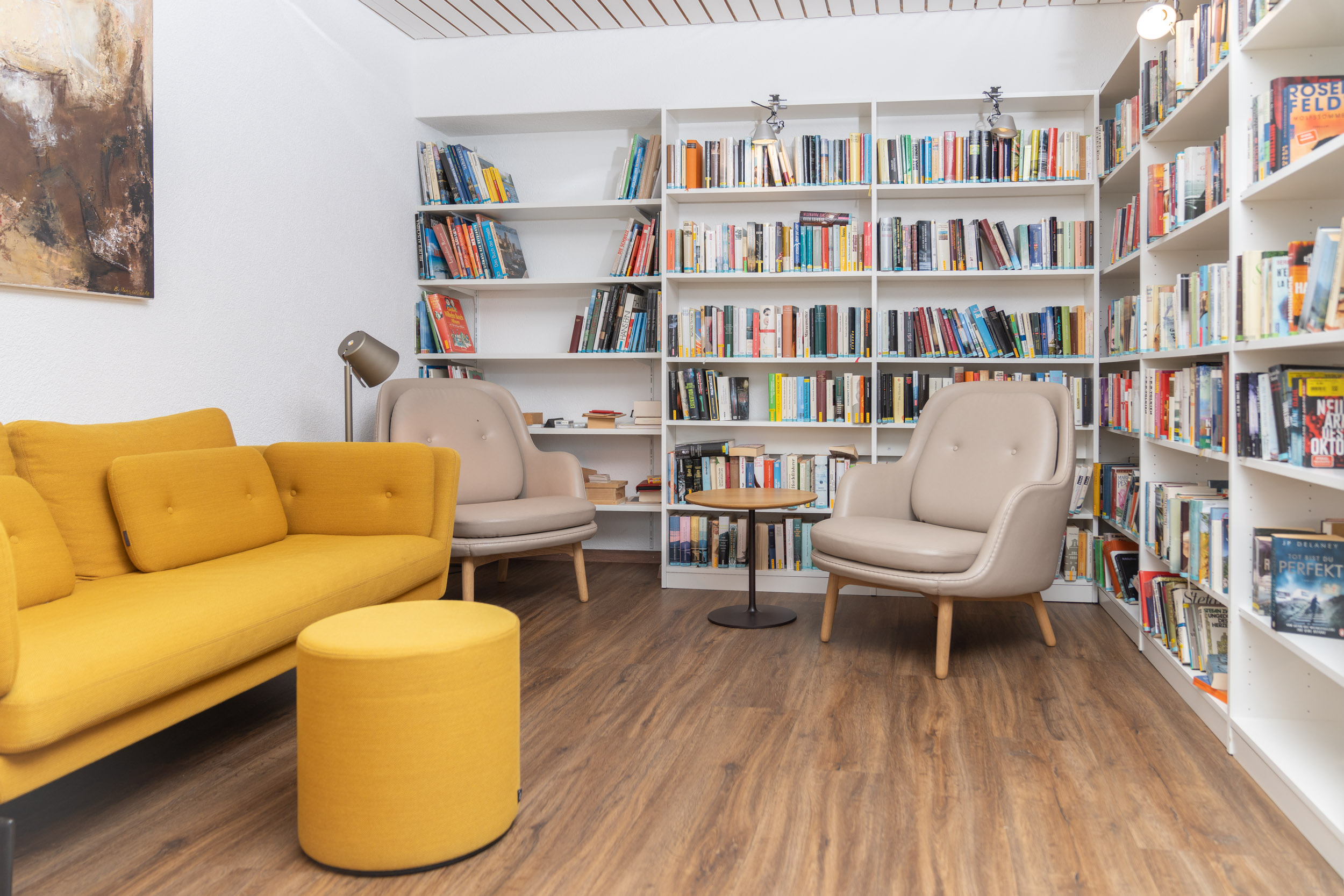 Leseraum mit Bücherregal, gelbem Sofa und beigen Ohrensesseln
