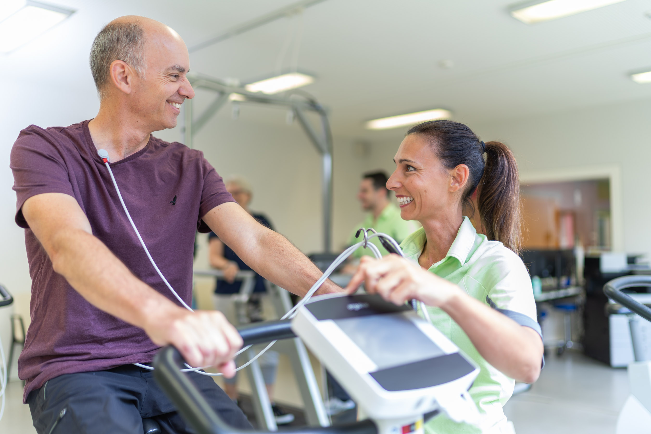 Patient auf dem Ergometer spricht mit Therapeutin