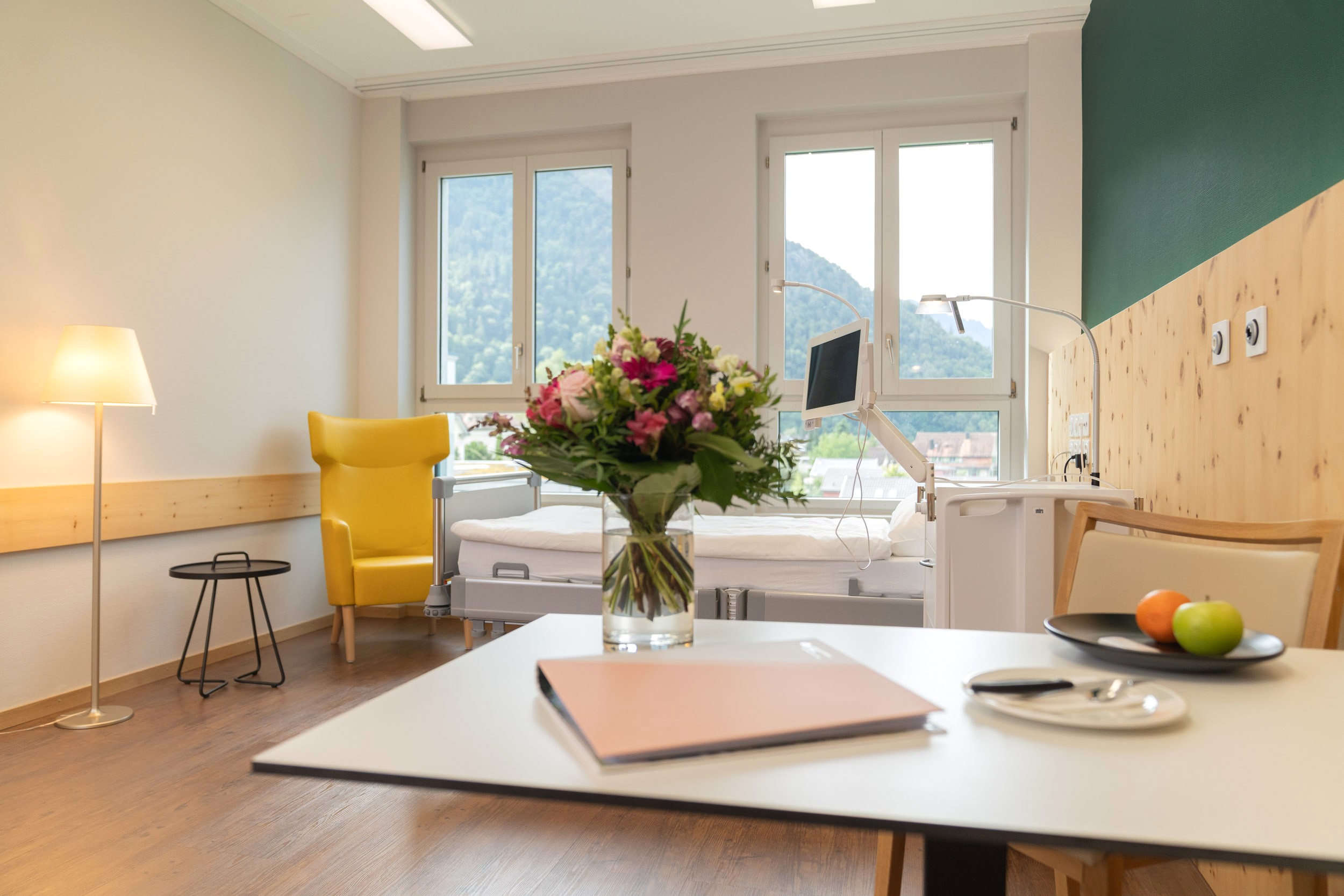 Patientenzimmer; im Vordergrund Tisch mit Blumenvase