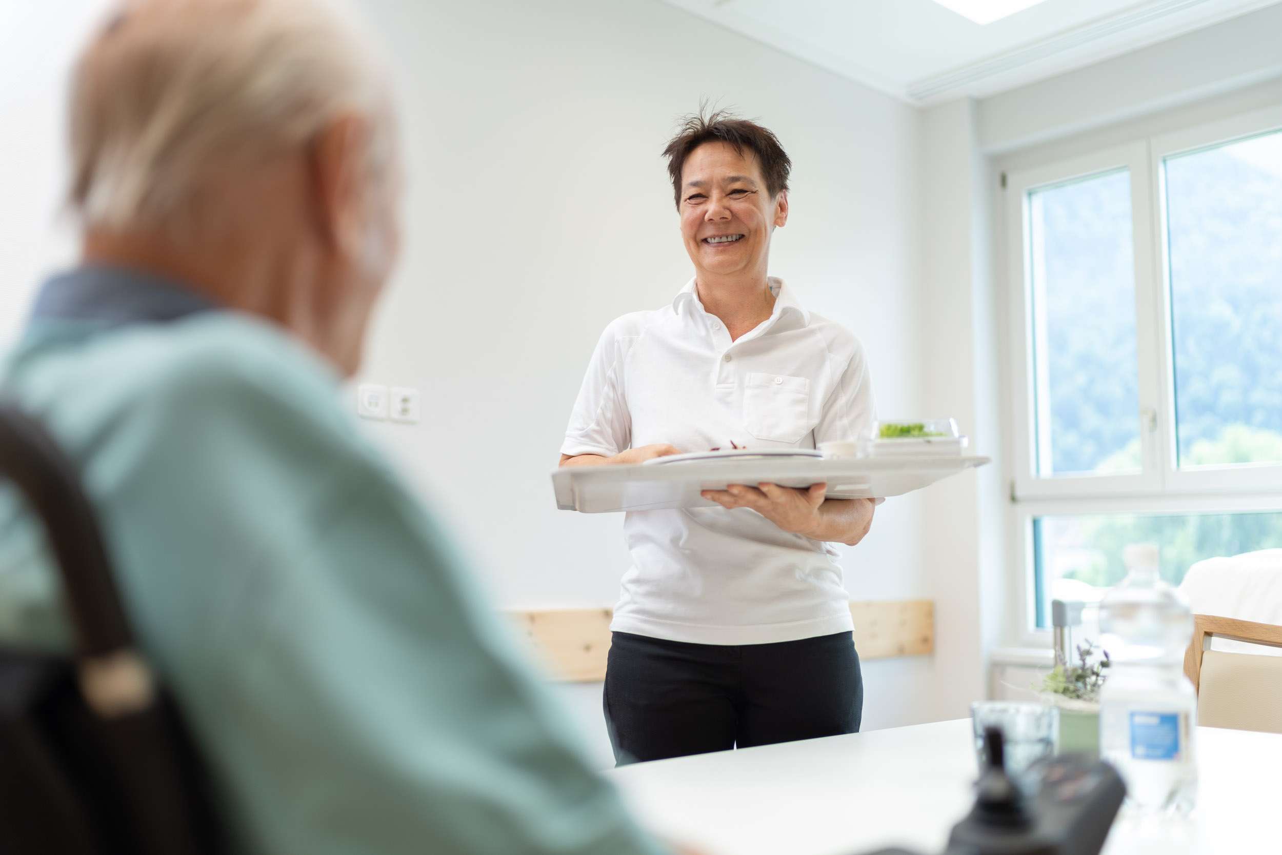 Servicemitarbeiterin bringt Patient Essen ins Zimmer