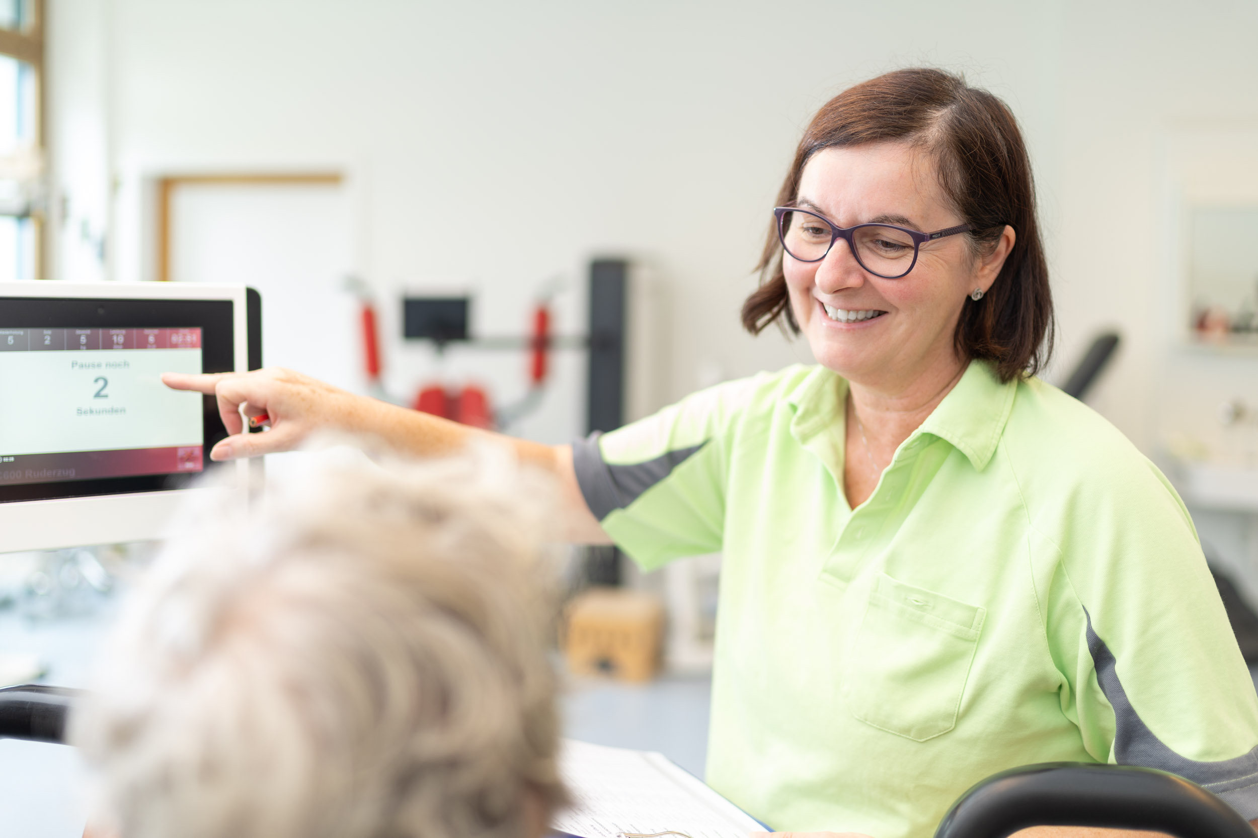 Therapeutin im Gespräch mit Patientin am Trainingsgerät
