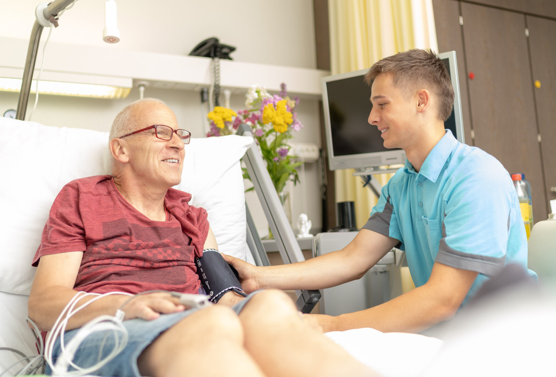Pfleger am Bett eines Patienten; misst den Blutdruck