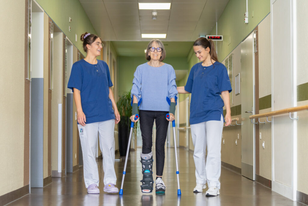 Zwei Pflegefachfrauen begleiten Patientin beim Gehen