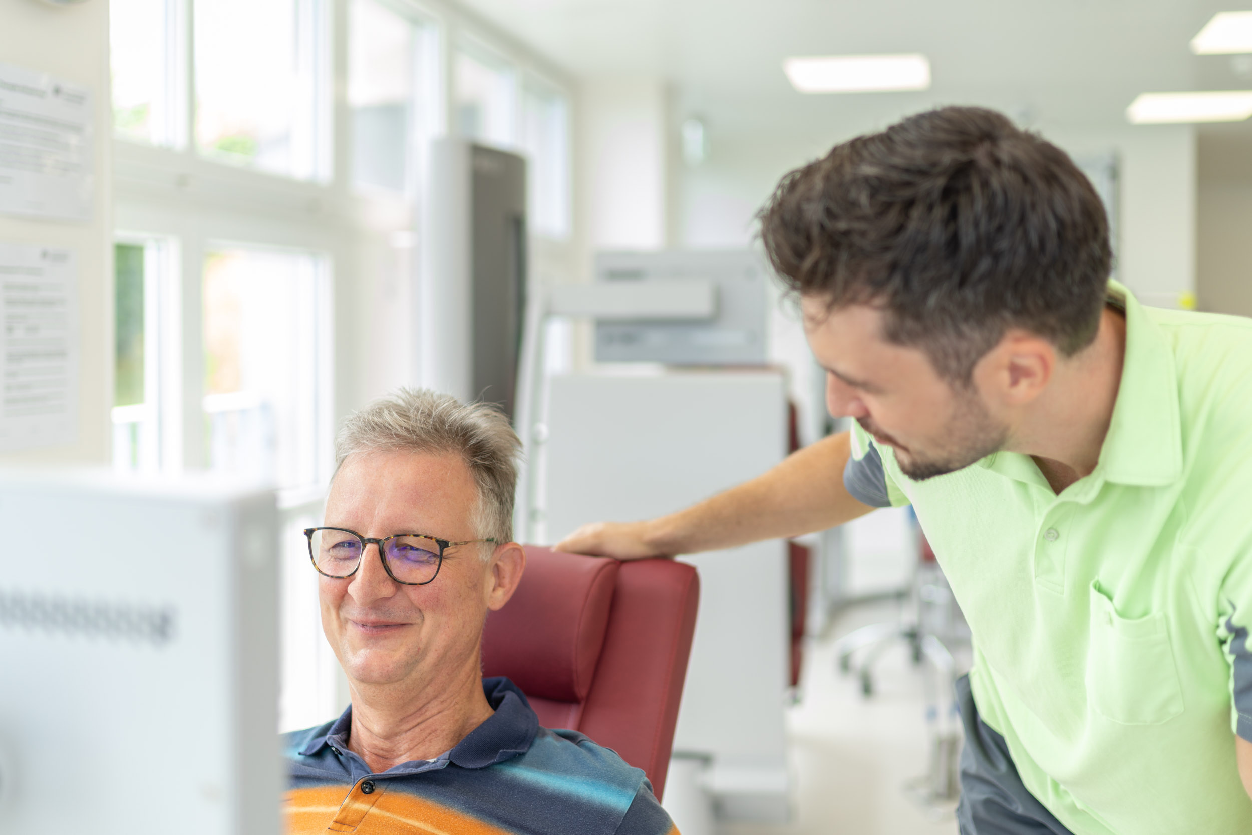 Therapeut spricht mit einem Patienten, der auf dem Ergometer sitzt