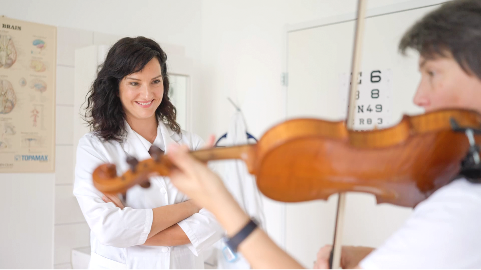 Ärztin schaut Patientin beim Geige spielen zu