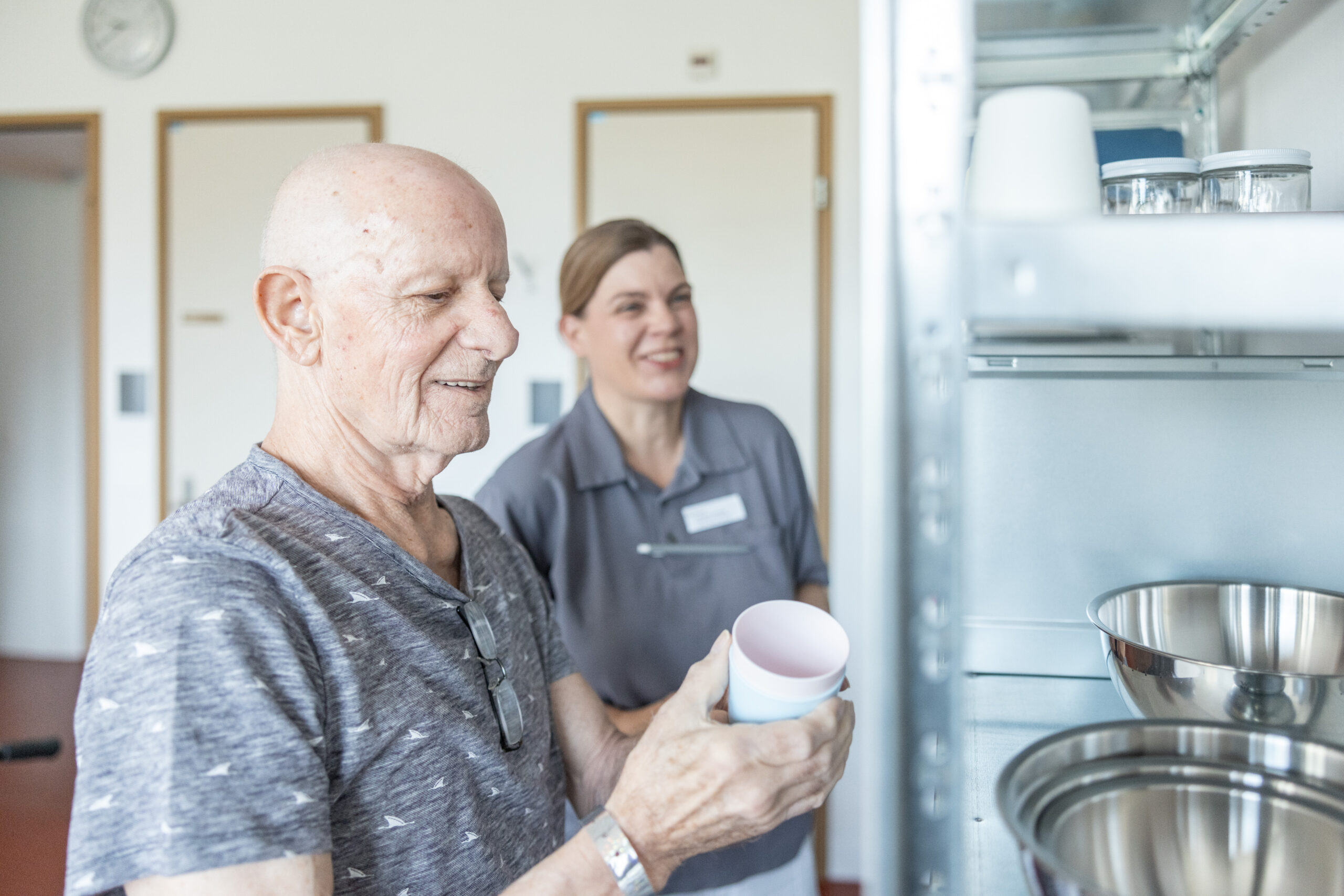 Patient nimmt Übungsmaterial von Regal, neben ihm eine Ergotherapeutin